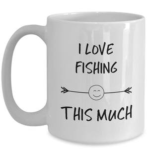 May include: White ceramic coffee mug with a black design that says "I love fishing this much" with a smiley face and arrows on either side.
