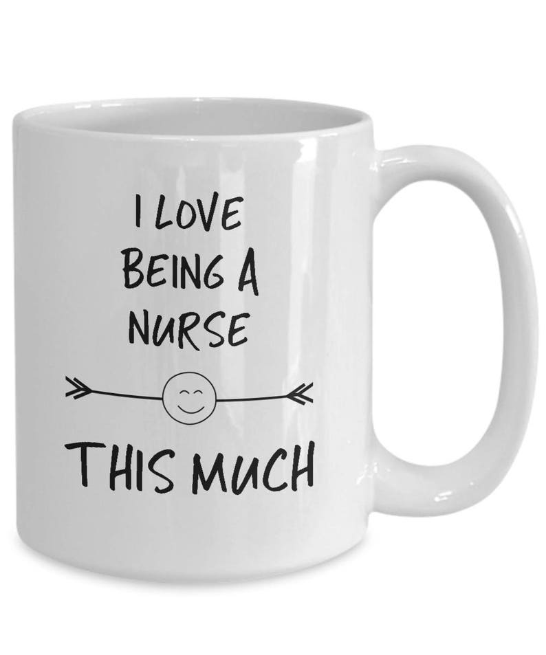 May include: White ceramic coffee mug with black text that reads "I love being a nurse this much" with a smiley face and arrows on either side.
