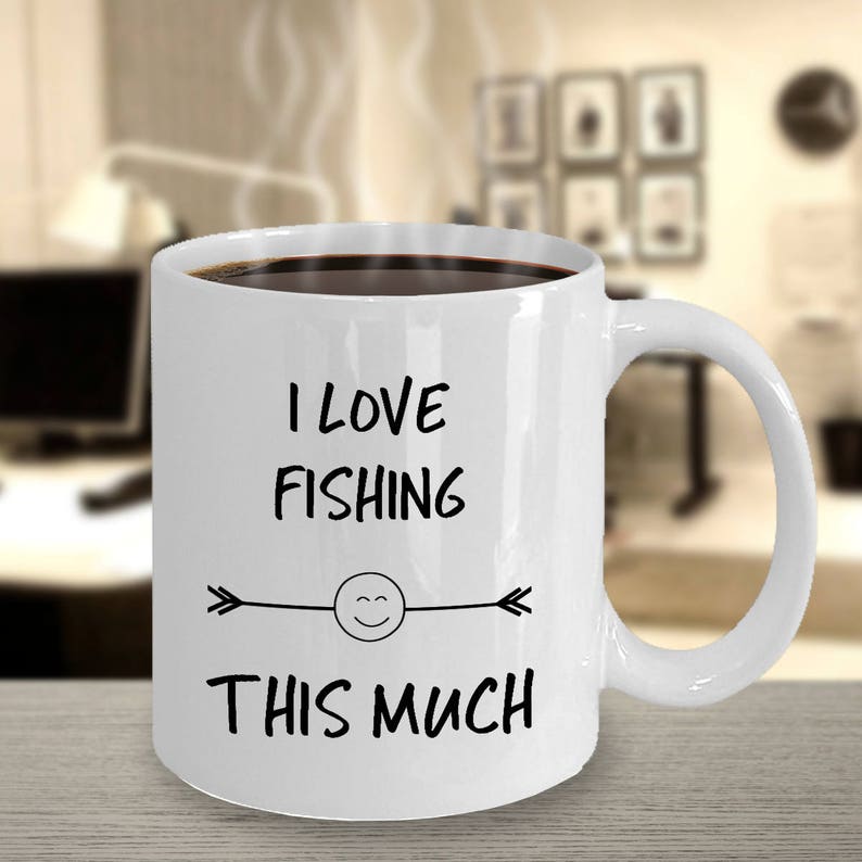 May include: White ceramic coffee mug with black text that reads "I love fishing this much" with a smiley face and arrows on either side of the smiley face.