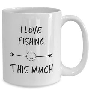 May include: White ceramic coffee mug with black text that reads "I love fishing this much" with a smiley face and arrows on either side.