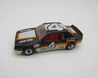 Puede incluir: Coche de juguete negro con detalles rojos y amarillos. El coche tiene el número 4 en el techo y en el lateral, y el texto "355 CID" y "Wells Racing" en el lateral.