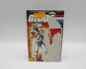 Puede incluir: Una tarjeta de figura de acción vintage para un personaje de G.I. Joe llamado "Cobra Commander". La tarjeta presenta un fondo rojo con un logotipo de G.I. Joe blanco y rojo. La figura se muestra en un traje de ninja blanco con una espada y un carcaj de flechas. La tarjeta también incluye el texto "FULLY POSEABLE MODERN ARMY FIGURE" y "AGES: 5 & UP".