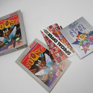 Peut inclure: Une cartouche de jeu Atari Joust vintage avec un dépliant Atari Special Offer argenté et bleu et un dépliant Atari 5200 argenté et blanc. La cartouche de jeu est dans une boîte blanche avec du texte rouge et bleu. Les dépliants ont un motif d'étoile avec un personnage de dessin animé.