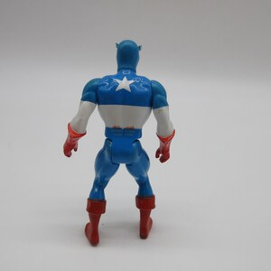 May include: A blue and red plastic action figure of Captain America. The figure is wearing a blue and white costume with a red star on the chest. The figure is standing with its arms at its sides.