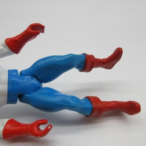 May include: A plastic action figure of a superhero wearing a blue and white costume with red boots and gloves. The figure is lying on its back with its legs spread apart.