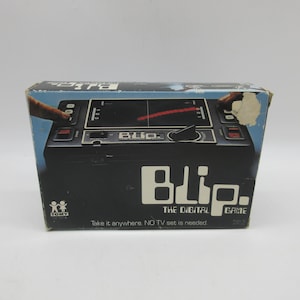 May include: A black and silver handheld electronic game called "BLip. The Digital Game." The game has a small screen and buttons. The box says "Take it anywhere. NO TV set is needed."