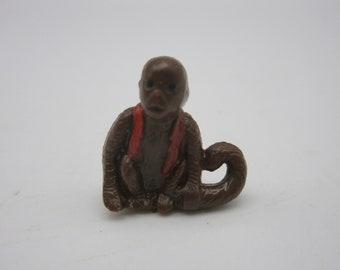 May include: A small brown monkey figurine with a red vest, sitting with its tail curled around its body.