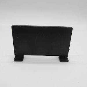 May include: A black, rectangular sign with a flat surface and two small, square feet. The sign is made of a solid, opaque material and stands upright. The background is plain white.