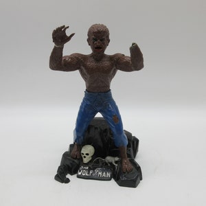 Peut inclure: Une figurine de loup-garou brun portant un jean bleu se tient sur une base de roche noire. La base est ornée d'un crâne et d'un petit rat, et le texte "THE WOLFMAN" y est inscrit.