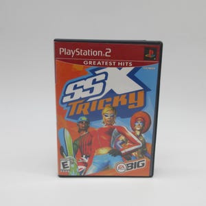 May include: A PlayStation 2 video game case for SSX Tricky Greatest Hits. The cover features three characters in winter sports gear, the game title in large blue and orange text, the EA Sports BIG logo, and an E rating symbol.