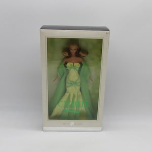 May include: A Barbie Collector doll in a box. The doll wears a light green gown with a matching shawl. The box has the words "Citrus" and "Barbie Collector" printed on it. The doll has blonde hair and is posed inside the box.