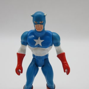 May include: A blue and red plastic action figure of Captain America. The figure has a white star on its chest and a red, white, and blue helmet.