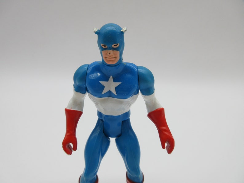 May include: A blue and red plastic action figure of Captain America. The figure has a white star on its chest and a red, white, and blue helmet.