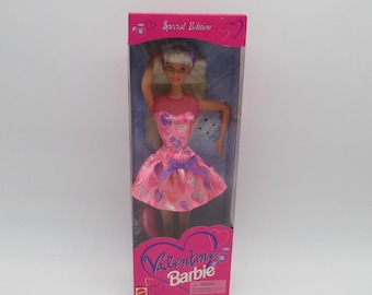 May include: A pink and purple Valentine's Day Barbie doll in a pink dress with hearts and a purple bow. The doll is in a clear plastic box with a pink and white background. The box says "Special Edition" and "Valentine Barbie".