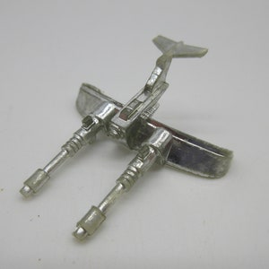 May include: A silver toy aeroplane with two cannons and a tail fin. The aeroplane is made of metal and has a shiny finish.