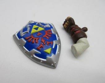 May include: A blue, silver, and red shield with a gold triangle and red bird emblem, next to a brown and tan arm. The shield has a silver border. The arm has a brown glove and a tan forearm.
