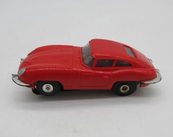 Pode incluir: Um pequeno carro de brinquedo vermelho com rodas pretas e acabamentos prateados. O carro clássico tem um design elegante com um teto curvo e é provavelmente um modelo vintage. O carro de brinquedo é uma réplica em miniatura de um carro esportivo.