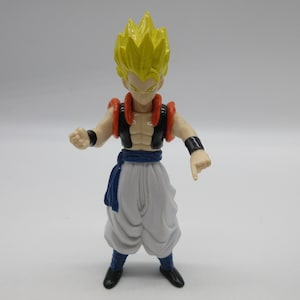 May include: A yellow-haired action figure with a white and blue outfit, orange and black armor, and a serious expression.