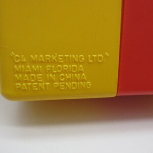 May include: Close-up of a yellow and red plastic container with the text "C4 MARKETING LTD." "MIAMI FLORIDA" "MADE IN CHINA" "PATENT PENDING" printed on the yellow side.