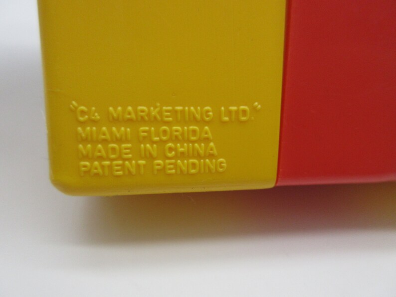 May include: Close-up of a yellow and red plastic container with the text "C4 MARKETING LTD." "MIAMI FLORIDA" "MADE IN CHINA" "PATENT PENDING" printed on the yellow side.