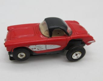 Pode incluir: Um pequeno carro de brinquedo vermelho com teto preto e para-brisa transparente. O carro tem detalhes prateados nas laterais e pneus pretos com aros prateados. Um carro de brinquedo clássico.