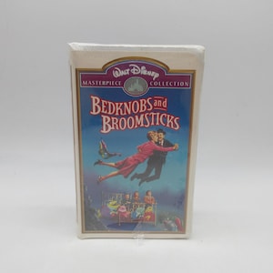 May include: A factory-sealed VHS tape of the Walt Disney Masterpiece Collection film Bedknobs and Broomsticks. The cover features a blue and purple background with an illustration of two people flying above three children sitting in a brass bed.