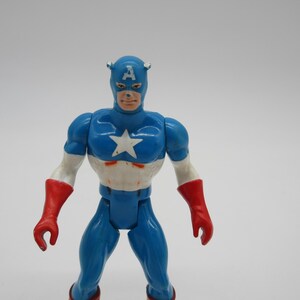 May include: A blue and red plastic action figure of Captain America. The figure has a white star on its chest and a red, white, and blue helmet with the letter "A" on the front.