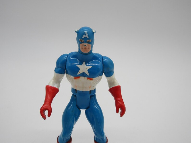 May include: A blue and red plastic action figure of Captain America. The figure has a white star on its chest and a red, white, and blue helmet with the letter "A" on the front.