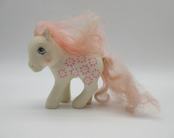 Op de afbeelding: Een wit My Little Pony speelgoed met roze haar en een roze en wit patroon. Het pony heeft blauwe ogen en een roze neus.
