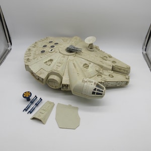 Puede incluir: Un modelo vintage de plástico blanco del  Millennium Falcon, la nave espacial de Star Wars. El modelo está desmontado e incluye varias piezas, como el cuerpo principal, una sección superior desmontable y dos paneles laterales. El modelo está en buen estado con algunos signos de desgaste.
