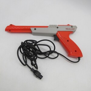 May include: A red and gray Nintendo Zapper light gun with a black cord and connector. The gun has a red barrel and handle, a gray body, and the Nintendo logo on the side. The cord is coiled.