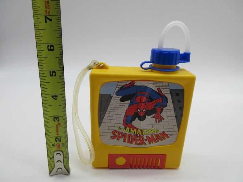 May include: Yellow plastic water bottle with a blue lid and a straw. The bottle has a picture of Spider-Man on the front with the text "The Amazing Spider-Man".