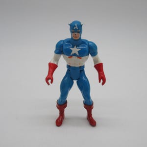 May include: A vintage action figure of Captain America, wearing his iconic blue and red costume with a white star on his chest. The figure has a red and white helmet with a blue 'A' on the front.