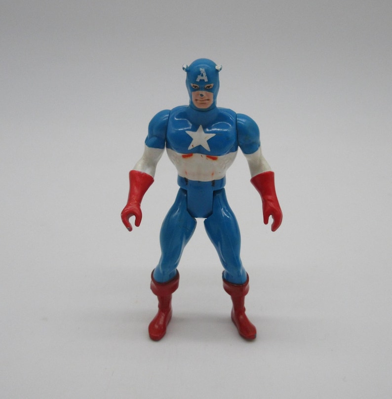 May include: A vintage action figure of Captain America, wearing his iconic blue and red costume with a white star on his chest. The figure has a red and white helmet with a blue 'A' on the front.