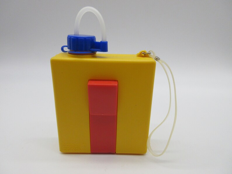 May include: A yellow plastic water bottle with a red and blue lid and a clear plastic strap. The bottle has a clear plastic straw attached to the lid.
