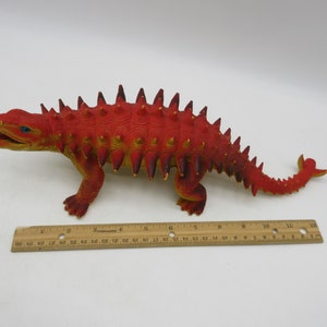 May include: Red and yellow plastic dinosaur toy with spikes on its back and tail. The dinosaur is about 11 inches long.