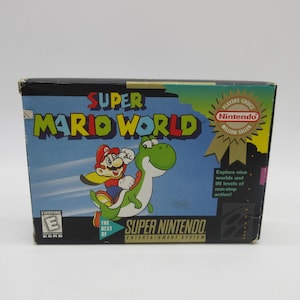 Puede incluir: Una caja rectangular de videojuego Super Mario World para el sistema Super Nintendo Entertainment. El frente muestra a Mario montando a Yoshi, el título, una clasificación ESRB E y un sello dorado de Players Choice Million Seller.