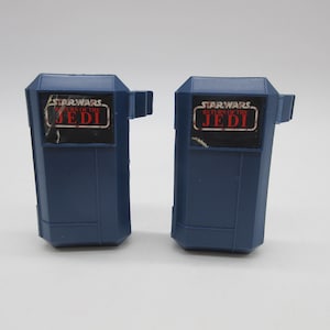 May include: Two blue plastic Star Wars Return of the Jedi toy accessories. Each has a rectangular shape with a small tab on the side and a sticker with the Star Wars logo and the word "Jedi".