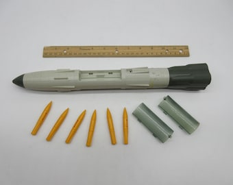 May include: A set of toy missiles, including a large grey and green missile with a removable nose cone and six smaller yellow missiles.