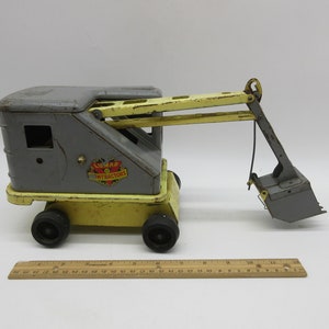 May include: A yellow and gray toy construction crane with a black bucket. The crane has a yellow base and a gray cab with the words "Lumar Contractors" printed on the side.