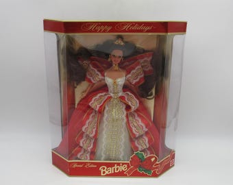 May include: A red and gold Barbie doll in a white gown with a red and gold bow. The doll is in a clear plastic box with a red and gold background. The box says "Happy Holidays" and "Special Edition Barbie".