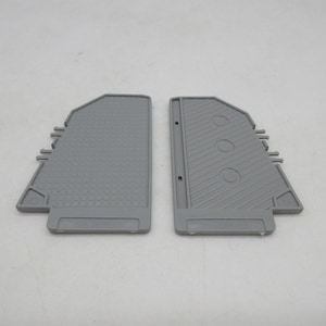 May include: Two gray plastic components with distinct surface textures. The left piece features a grid pattern, while the right piece has diagonal lines and three circular indentations. Both items include side tabs and molded geometric details.