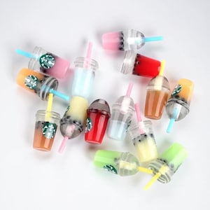 Pu&ograve; includere: Una collezione di mini bevande al t&egrave; alle bolle in vari colori, tra cui rosa, arancione e verde. Ogni bevanda ha una cannuccia e un logo Starbucks. Le bevande sono disposte su una superficie bianca.