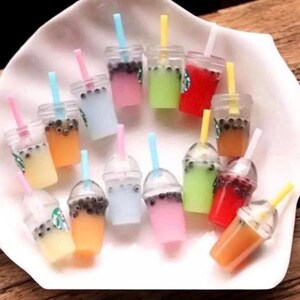 Pu&ograve; includere: Miniature bevande al bubble tea colorate con cannucce. Le bevande sono in bicchieri di plastica trasparente con vari colori pastello, tra cui rosa, blu, verde e arancione. Alcune tazze hanno un logo Starbucks.