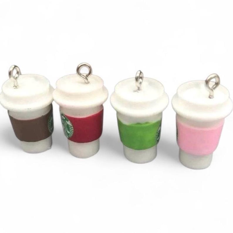 May include: Four miniature coffee cup charms with white lids and colorful sleeves. The sleeves are brown, red, green, and pink. Each charm has a silver loop at the top for attaching to jewelry or other crafts.