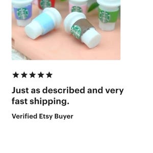 May include: Miniature coffee cups in various colors, including blue, red, pink, and green, with white lids. The cups have a logo design and are arranged on a light pink surface, with green foliage in the background.