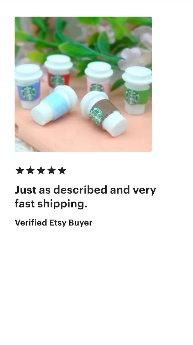 May include: Miniature coffee cups in various colors, including blue, red, pink, and green, with white lids. The cups have a logo design and are arranged on a light pink surface, with green foliage in the background.