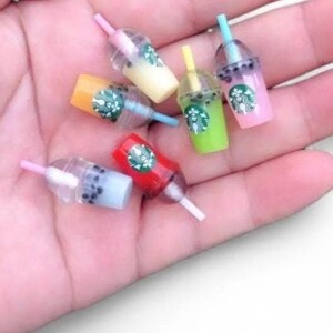 Pu&ograve; includere: Miniature tazze colorate di bubble tea con cannucce. Le tazze sono in vari colori, tra cui rosa, verde, giallo e rosso. Ogni tazza ha un logo Starbucks.