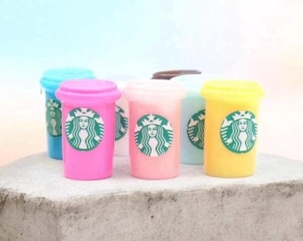May include: A collection of miniature plastic cups in various pastel colors including pink, yellow, blue, and white. Each cup features the green and white Starbucks siren logo printed on the front, with a matching lid on top of each container.