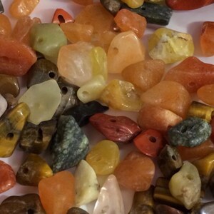 May include: A collection of polished gemstones in various colors, including orange, yellow, green, and red. The stones have irregular shapes and are drilled with holes for stringing. The gemstones are suitable for jewelry making or crafting.